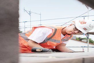 Auszubildende mit Sicherheitsausrüstung auf der Baustelle hammert auf eine Mauer