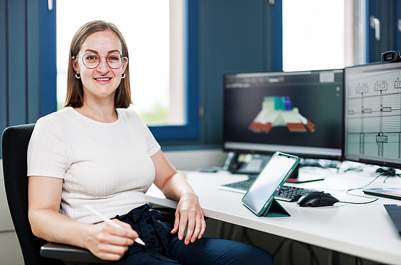 Ausbildende sitzt am PC und lächelt in die Kamera