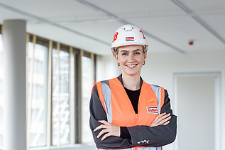 Foto von einer jungen Frau auf der Baustelle, die in die Kamera lächelt