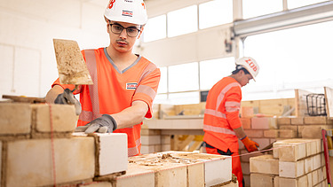 Auszubildender in der Konzernlehrwerkstatt, der gerade Steine aufeinandersetzt.