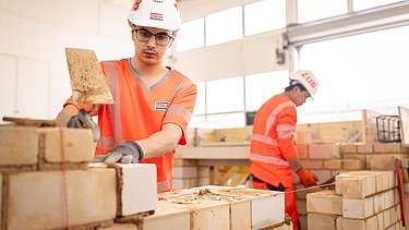 Auszubildender in der Konzernlehrwerkstatt, der gerade Steine aufeinandersetzt.