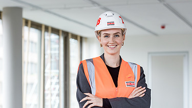 Foto von einer jungen Frau auf der Baustelle, die in die Kamera lächelt