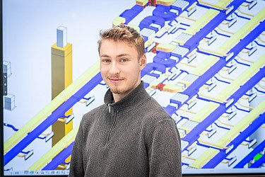 Foto eines Azubis, der vor einem TGA-Bauplan ist
