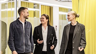 Drei Kolleg:innen laufen einen Gang entlang