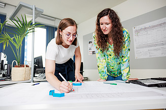 Zwei Mitarbeiterinnen beugen sich vor einen Bauplan