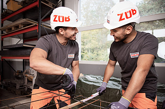 Zwei Bauarbeiter lächseln sich an.