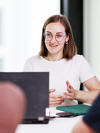 Eine junge Kollegin sitzt in einer Sprechung am Laptop.