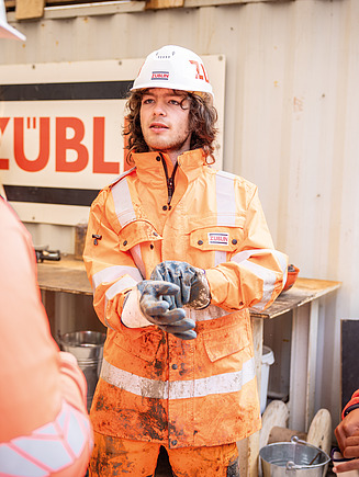 Bild eines Azubi in Schützausrüstung mit seinem Team auf einer Baustelle.