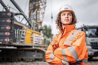 Bild eines Azubis, der vor einem Bagger steht.