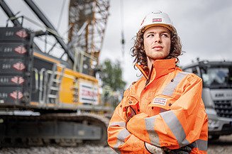 Bild eines Azubis, der vor einem Bagger steht.