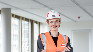 Foto von einer jungen Frau auf der Baustelle, die in die Kamera lächelt