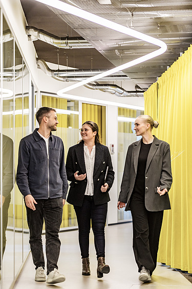 Drei Kolleg:innen laufen einen Gang entlang
