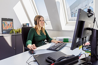 Foto einer kaufmännischen Mitarbeiterin an ihrem Schreibtisch vor dem PC