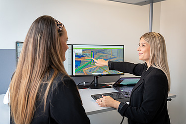 Foto eines Azubis, der vor einem Bagger kniet.