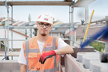 Bild eines Azubis mit Schutzhelm und Schutzhandschuhen blickt in die Kamera