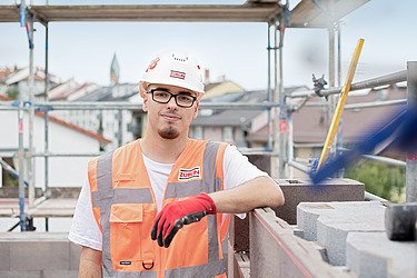 Bild eines Azubis mit Schutzhelm und Schutzhandschuhen blickt in die Kamera