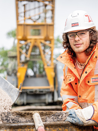 Foto eines Azubis, der vor einer Baumaschine kniet.
