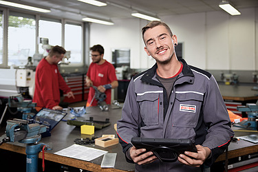Bild eines Azubis, der ein Tablet in der Hand hält und lächelt
