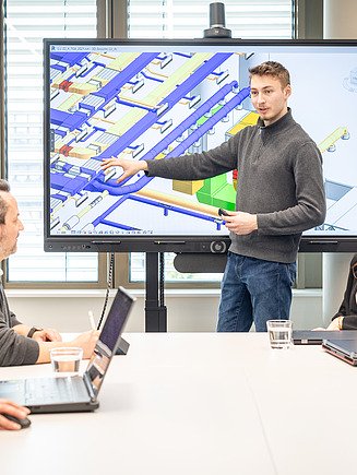 Bild von einem Mann, der an seinem Büroarbeitsplatz vor zwei Bildschirmen an einem Bauplan arbeitet.