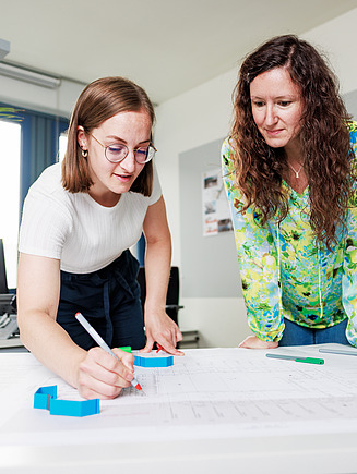 Zwei Kolleginnen zeichnen an einem Bauplan.