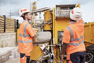 Bild von zwei Auszubildenden, die gerade eine Baumaschine warten.